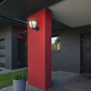 Außenansicht eines modernen Hauses mit einer Akku-Außenwandleuchte an einer roten Wand, seitliche Perspektive.