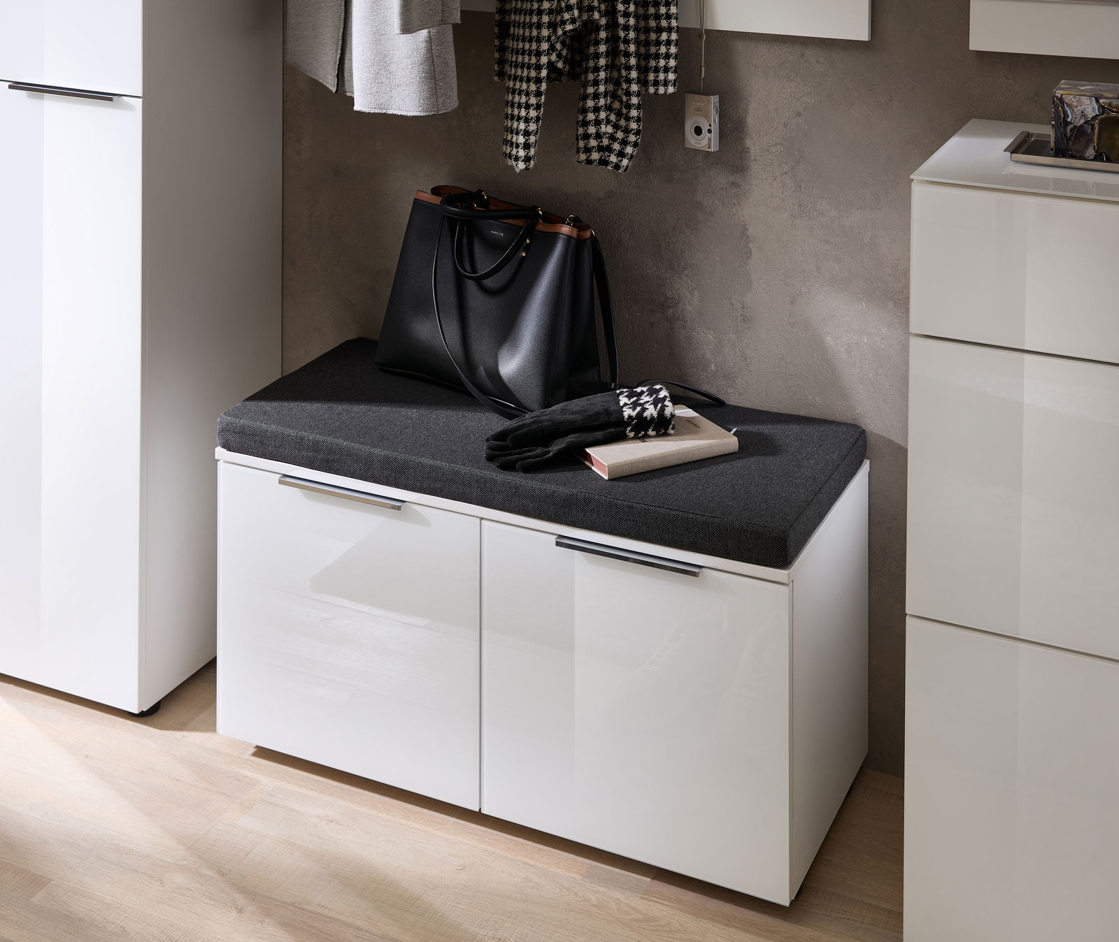 Weiße Bank mit schwarzem Sitzpolster, darauf eine schwarze Tasche und ein Buch, seitliche Perspektive.