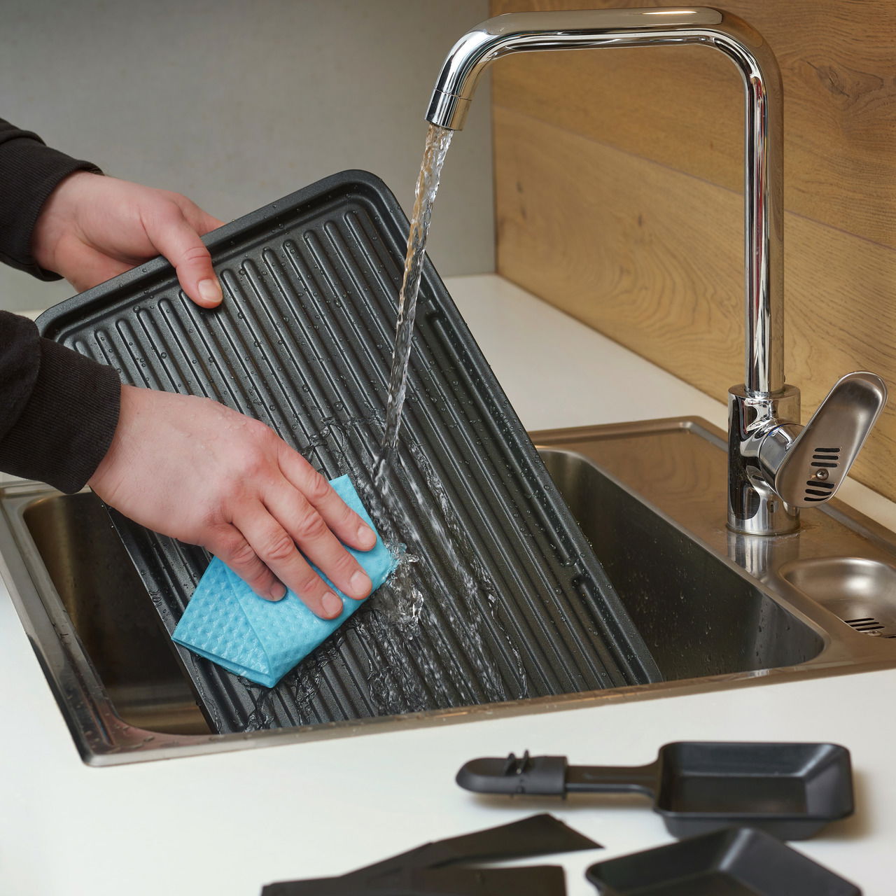 Reinigung einer Raclette-Grillplatte unter fließendem Wasser in der Küche, Nahaufnahme