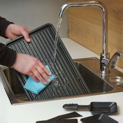 Reinigung einer Raclette-Grillplatte unter fließendem Wasser in der Küche, Nahaufnahme