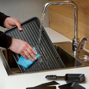 Reinigung einer Raclette-Grillplatte unter fließendem Wasser in der Küche, Nahaufnahme