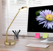 Elegante LED-Tischleuchte in Gold auf einem Schreibtisch, seitliche Perspektive, neben einem Computerbildschirm mit einer Blume.