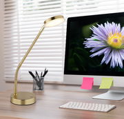 Elegante LED-Tischleuchte in Gold auf einem Schreibtisch, seitliche Perspektive, neben einem Computerbildschirm mit einer Blume.