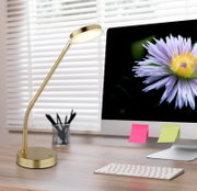 Elegante gouden led-tafellamp op een bureau, gezien vanaf de zijkant, naast een computerscherm met een bloem.