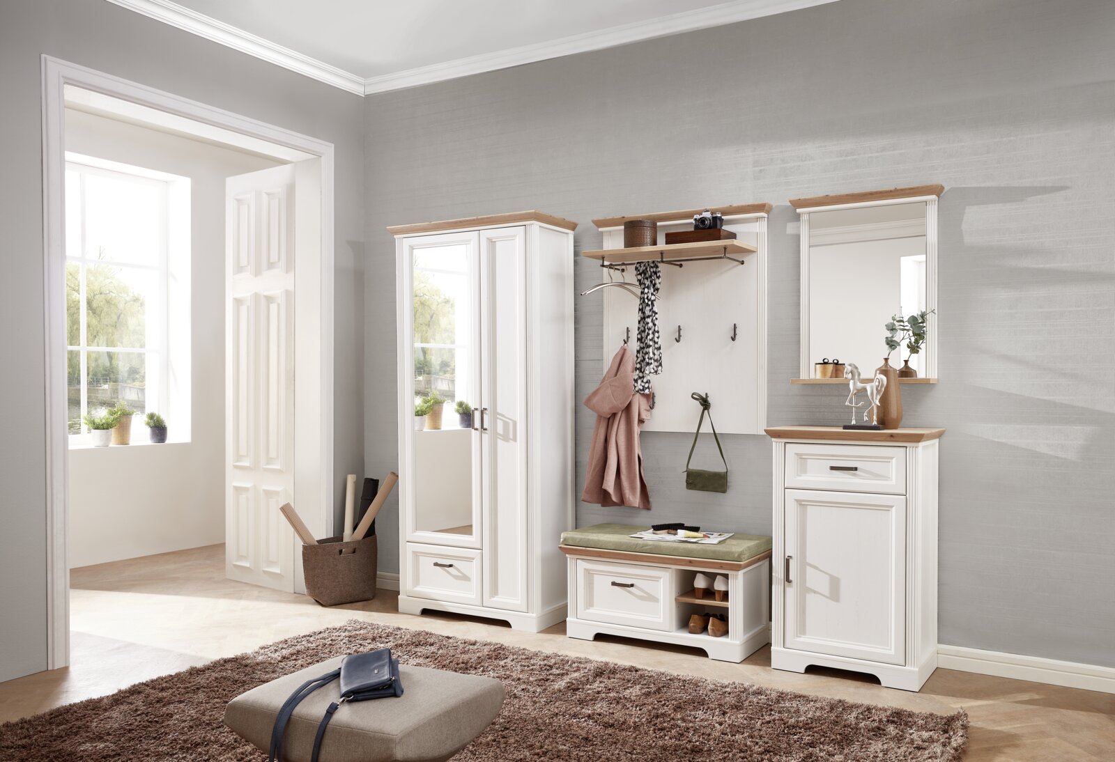 Garderoben-Set in einem modernen Flur mit weißem Holz und naturfarbenen Akzenten, bestehend aus einem hohen Schrank mit Spiegel, einer Sitzbank mit Stauraum und einem Wandpaneel mit Haken, aus der Perspektive des Raumes fotografiert.