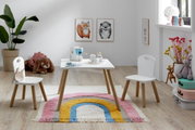 Heller Kinderzimmer-Spielbereich mit weißem Kindertisch und zwei passenden Stühlen mit Holzbeinen auf Regenbogen-Teppich, frontal aus leicht erhöhter Perspektive aufgenommen.