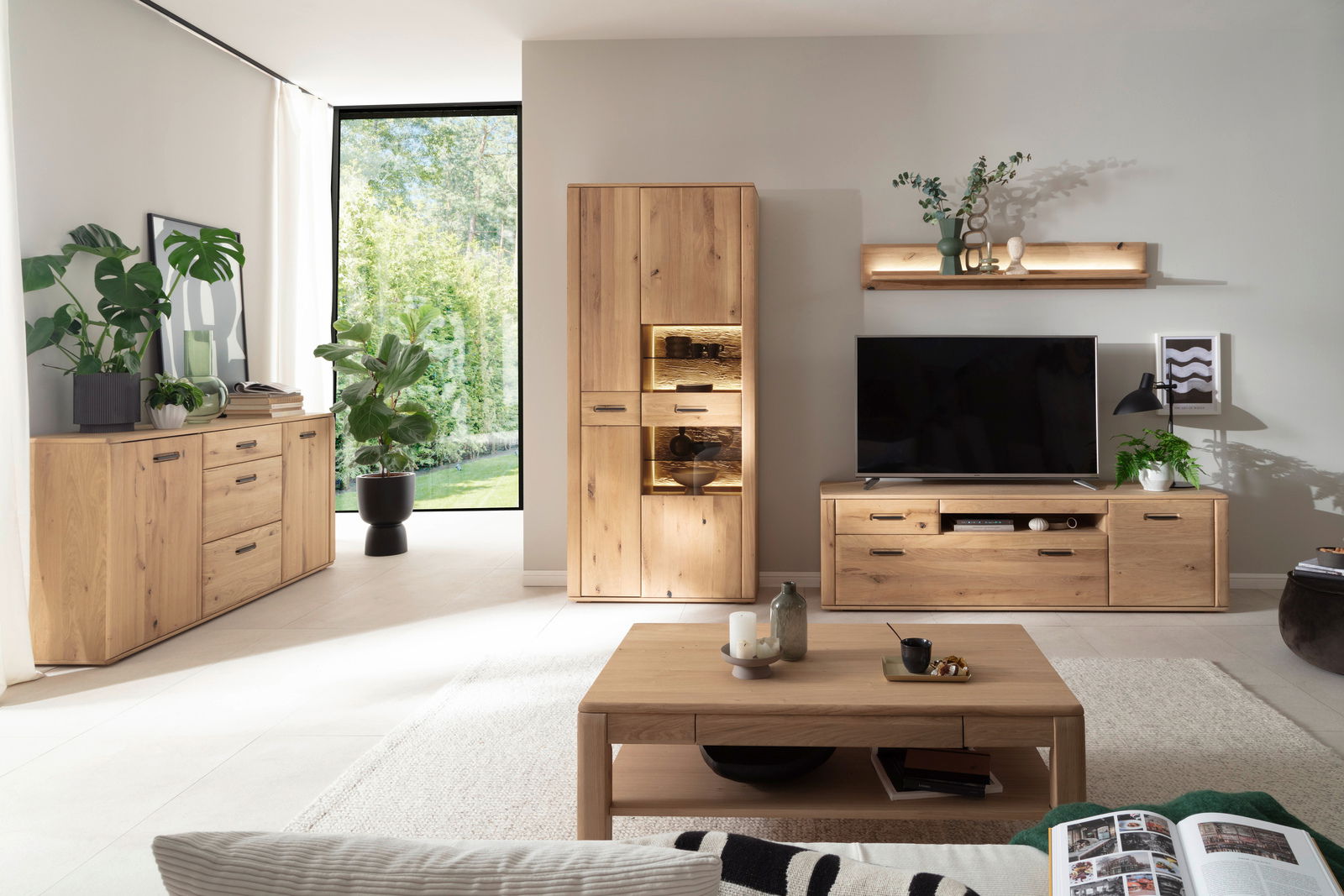 Moderne Wohnzimmer-Wandkombination aus Holz mit TV-Schrank, Vitrine und Regal, aus der Perspektive eines gemütlichen Wohnzimmers mit Blick auf eine große Fensterfront.