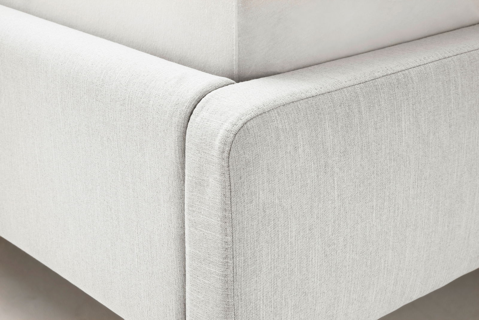 Nahaufnahme eines Polsterbetts in hellem Stoff, Ecke des Bettrahmens aus seitlicher Perspektive.