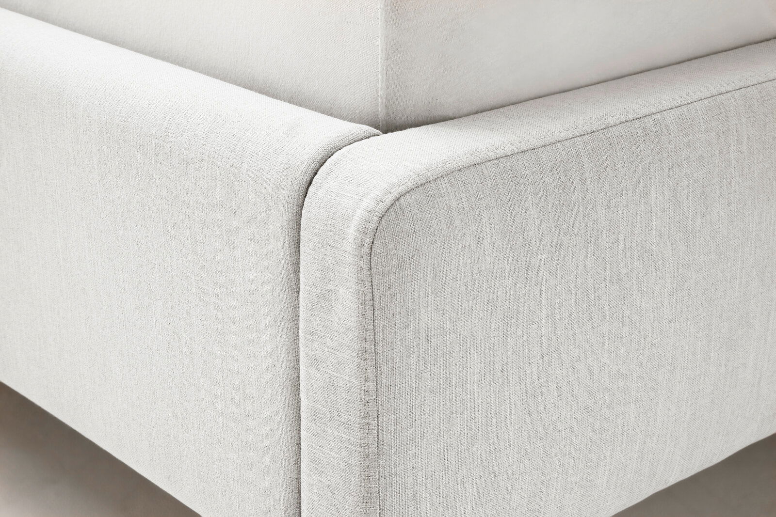 Nahaufnahme eines Polsterbetts in hellem Stoff, Ecke des Bettrahmens aus seitlicher Perspektive.