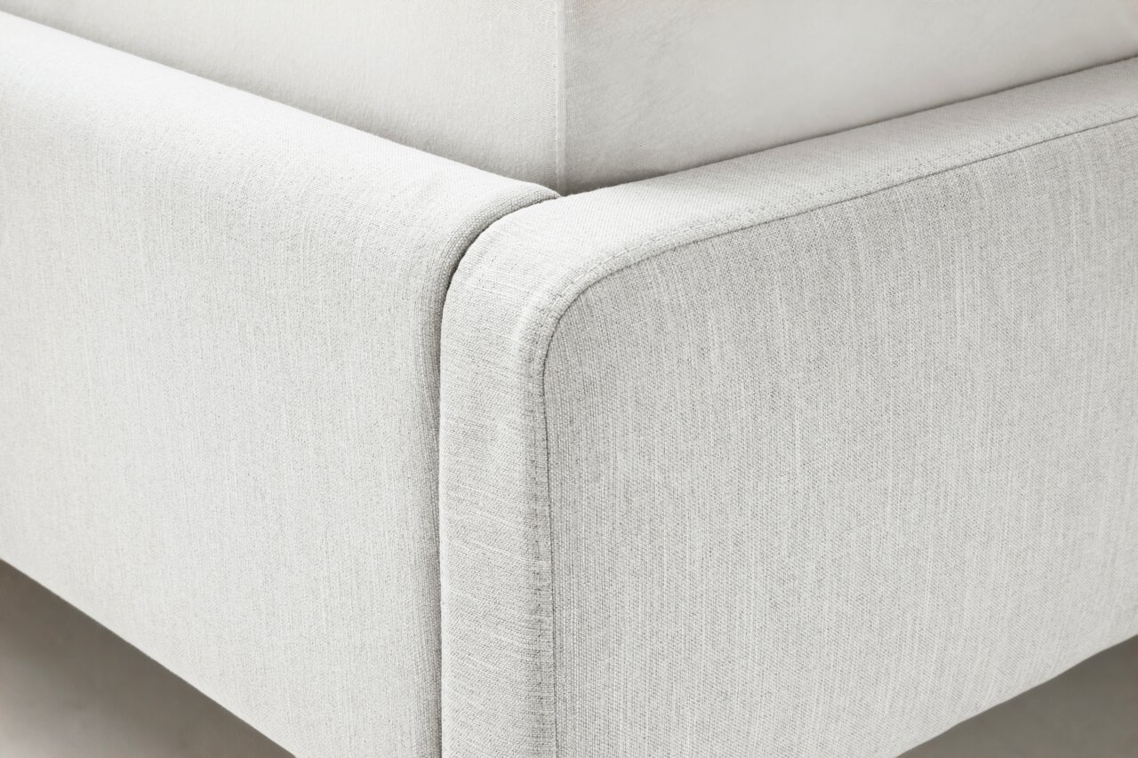 Nahaufnahme eines Polsterbetts in hellem Stoff, Ecke des Bettrahmens aus seitlicher Perspektive.