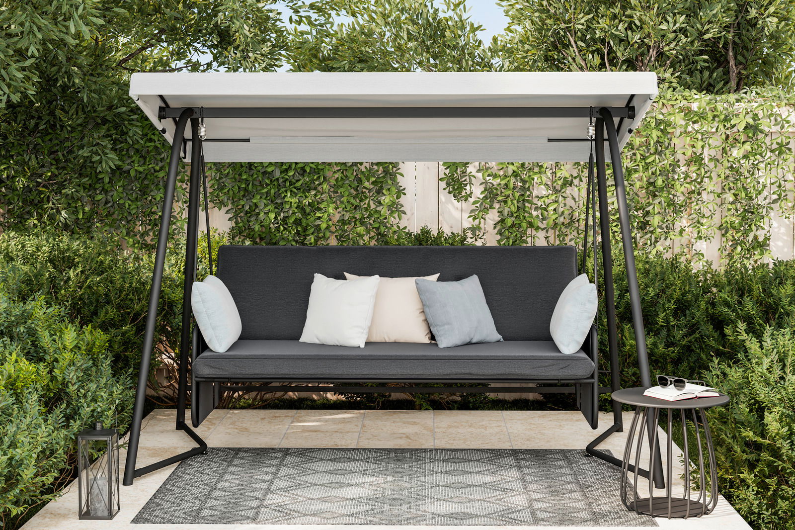 Hollywoodschaukel im Garten mit grauem Sitzpolster und Kissen, umgeben von grünen Büschen und Bäumen, aus frontaler Perspektive.