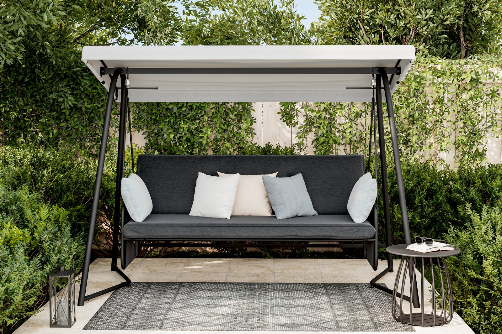 Hollywoodschaukel im Garten mit grauem Sitzpolster und Kissen, umgeben von grünen Büschen und Bäumen, aus frontaler Perspektive.