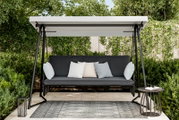 Hollywoodschaukel im Garten mit grauem Sitzpolster und Kissen, umgeben von grünen Büschen und Bäumen, aus frontaler Perspektive.