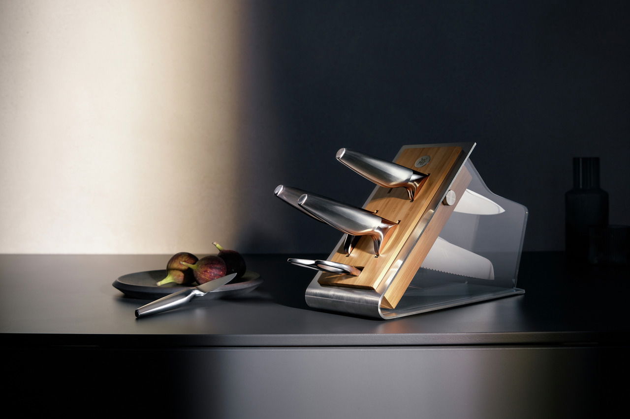 Moderner Messerblock aus Holz und Metall mit drei Messern, seitliche Perspektive, auf einer dunklen Küchenarbeitsplatte.