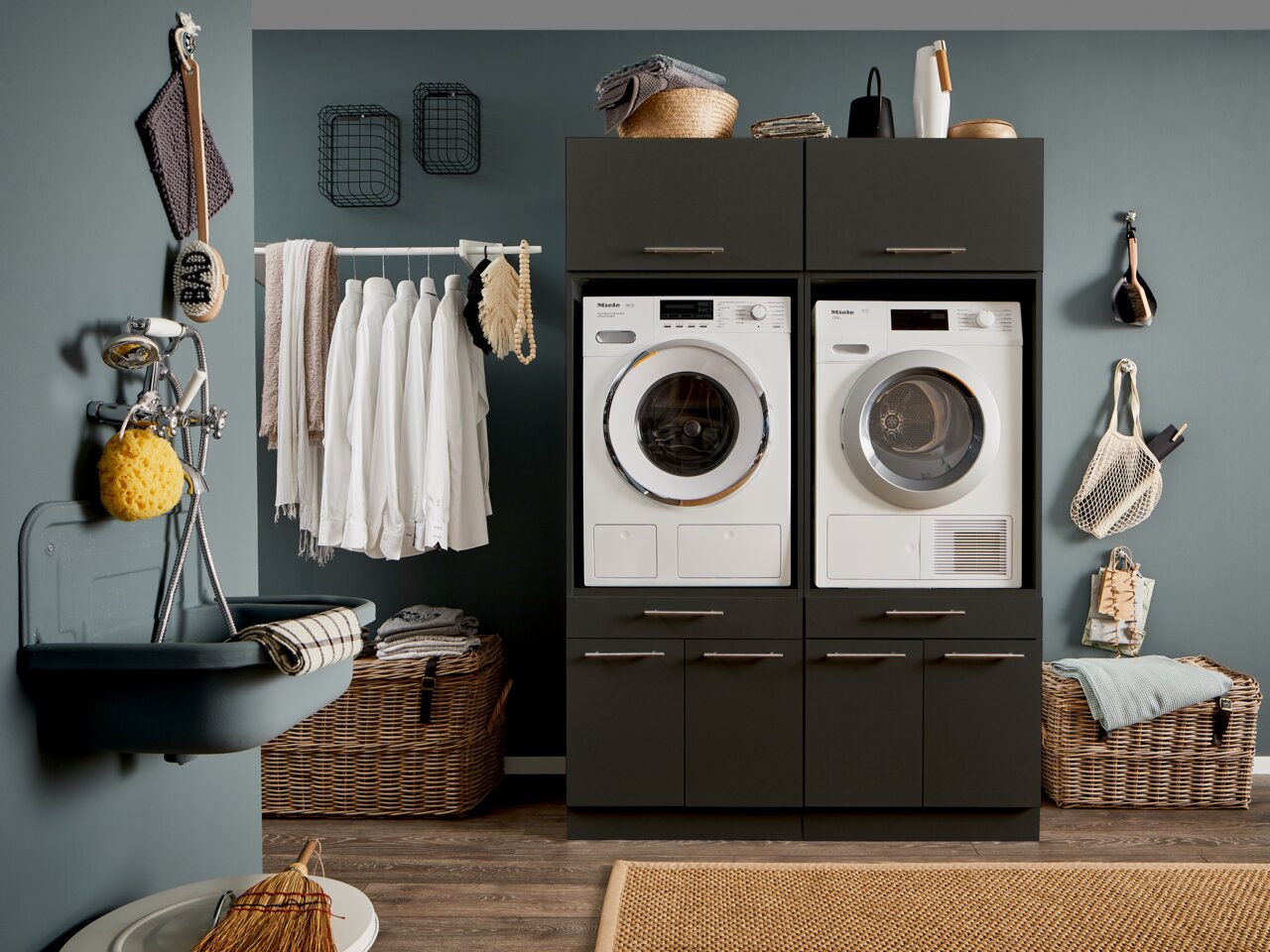 Moderne Waschküche mit dunklen Schränken, Waschmaschine und Trockner in Frontansicht, umgeben von Wäschekörben und Accessoires.