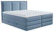 Lichtblauw gestoffeerd tweepersoons boxspringbed met hoog, verticaal gecapitonneerd hoofdbord en witte doorgestikte topper, schuin van voren bekeken