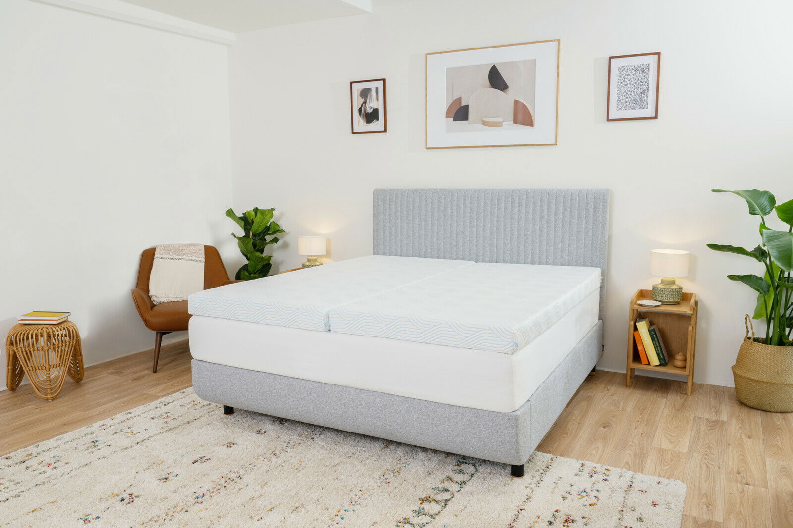 Schlafzimmer mit einem grauen Bett mit Topper, umgeben von Pflanzen und moderner Dekoration, seitliche Perspektive