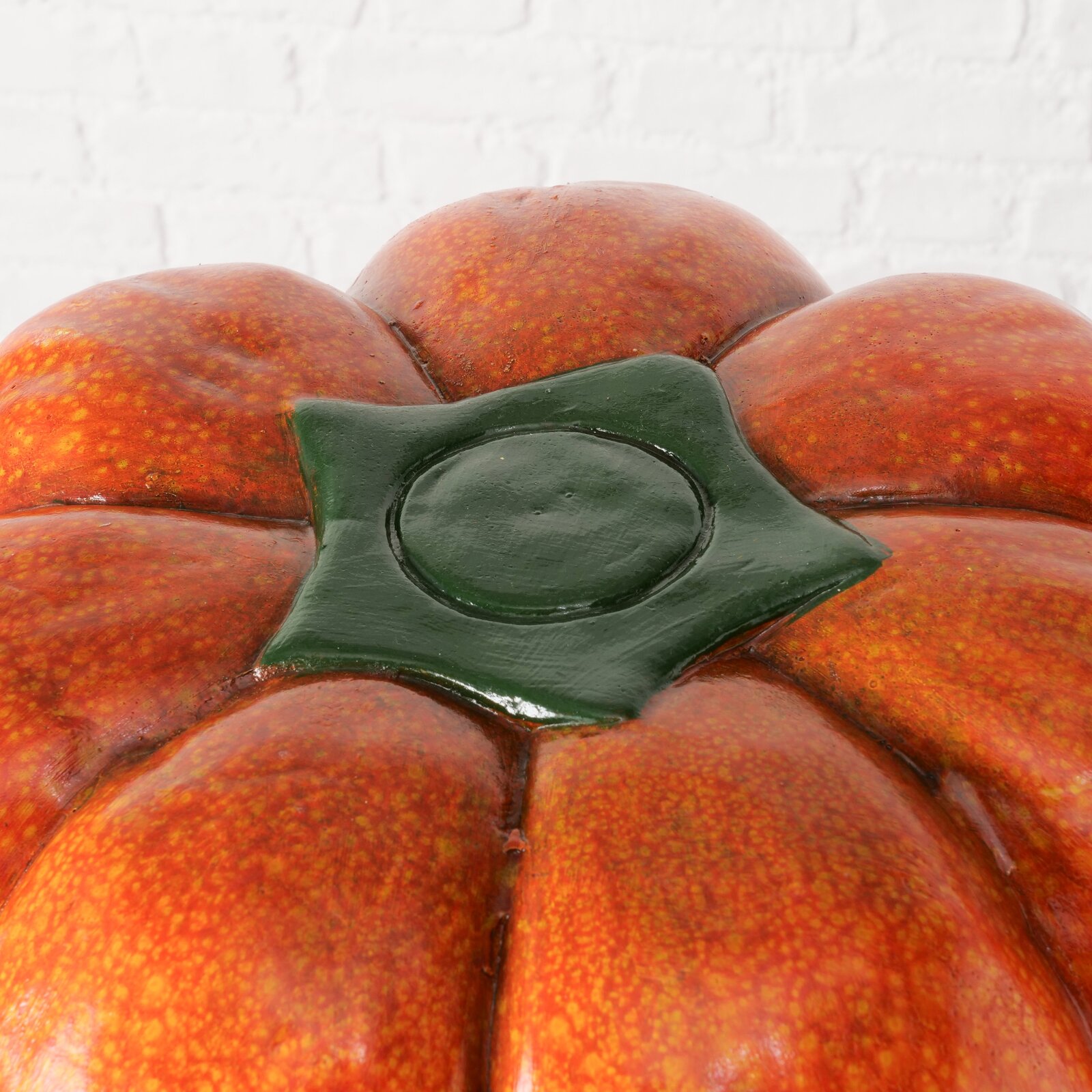 Nahaufnahme eines Hockers in Form eines Kürbisses mit oranger Oberfläche und grünem Stiel, von oben betrachtet.