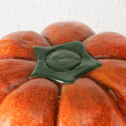 Nahaufnahme eines Hockers in Form eines Kürbisses mit oranger Oberfläche und grünem Stiel, von oben betrachtet.