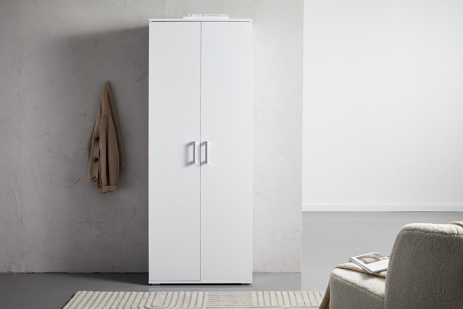 XORA XL-Schuhschrank ALEX Weißer XL-Schuhschrank mit zwei Türen, frontal fotografiert, neben einer grauen Wand mit hängendem Mantel.