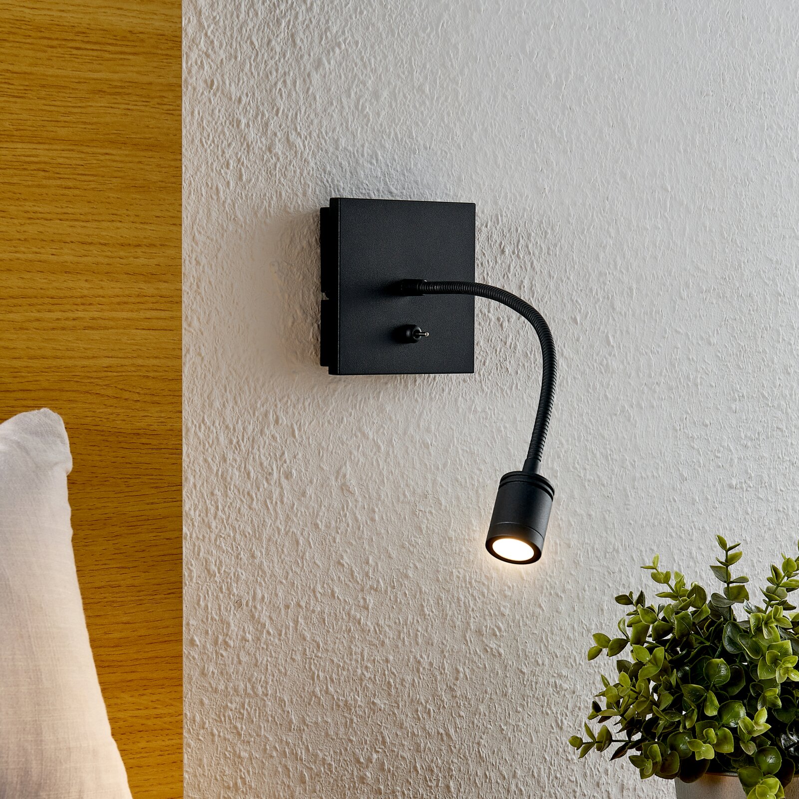 Schwarze, minimalistische LED-Wandleuchte mit flexiblem Schwanenhals und kleinem Spot an strukturierter weißer Wand, seitliche Perspektive mit leichtem Blick von oben