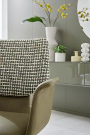 Detailansicht eines Sessels mit gemustertem Stoffbezug und eleganter Form, im Hintergrund moderne Dekorationselemente.