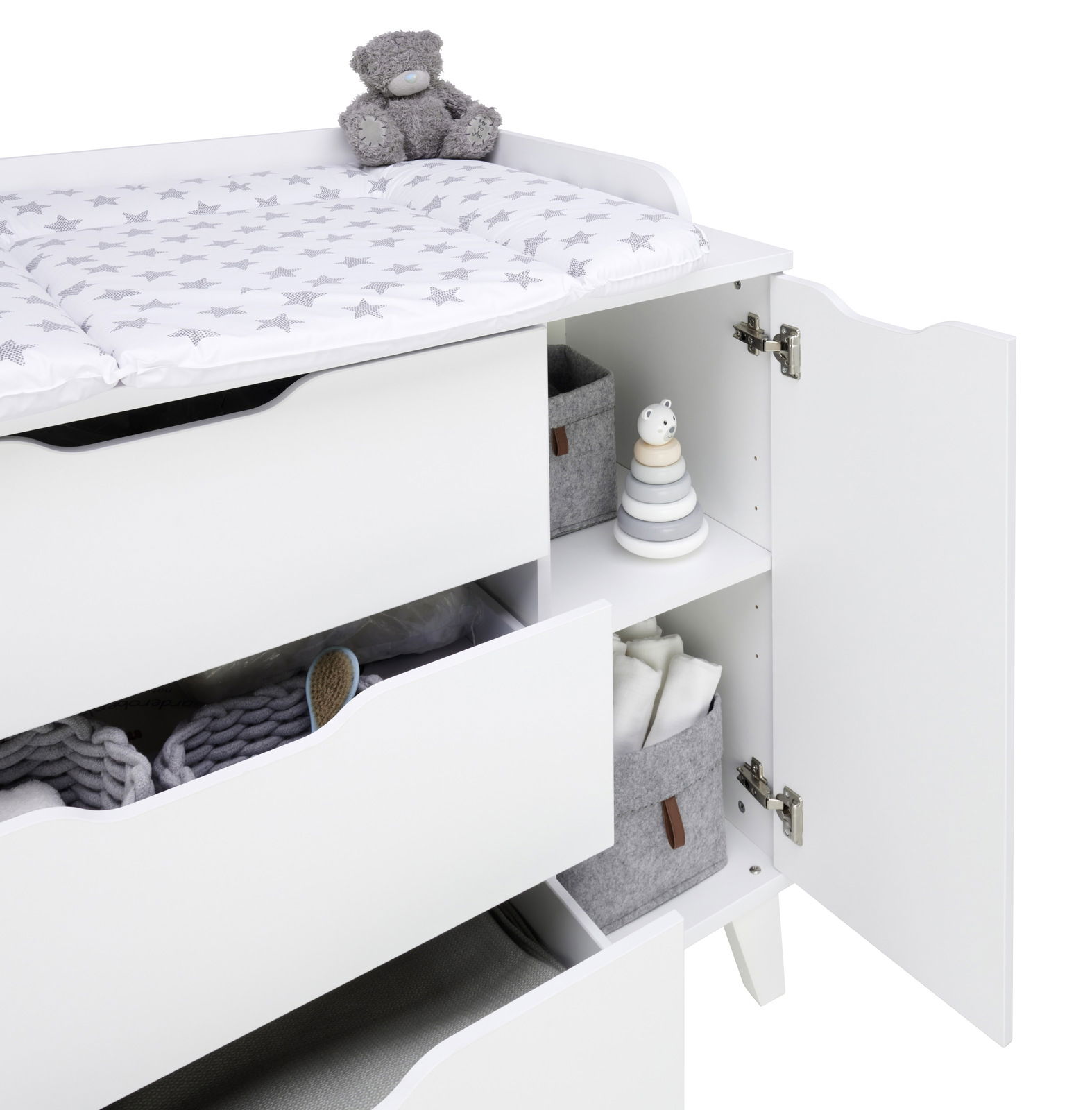 Weiße Wickelkommode mit offenen Schubladen und Türen, von der Seite betrachtet, mit einem Plüschbären und einem Wickelpolster mit Sternenmuster.