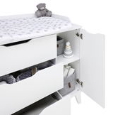 Weiße Wickelkommode mit offenen Schubladen und Türen, von der Seite betrachtet, mit einem Plüschbären und einem Wickelpolster mit Sternenmuster.