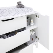 Weiße Wickelkommode mit offenen Schubladen und Türen, von der Seite betrachtet, mit einem Plüschbären und einem Wickelpolster mit Sternenmuster.