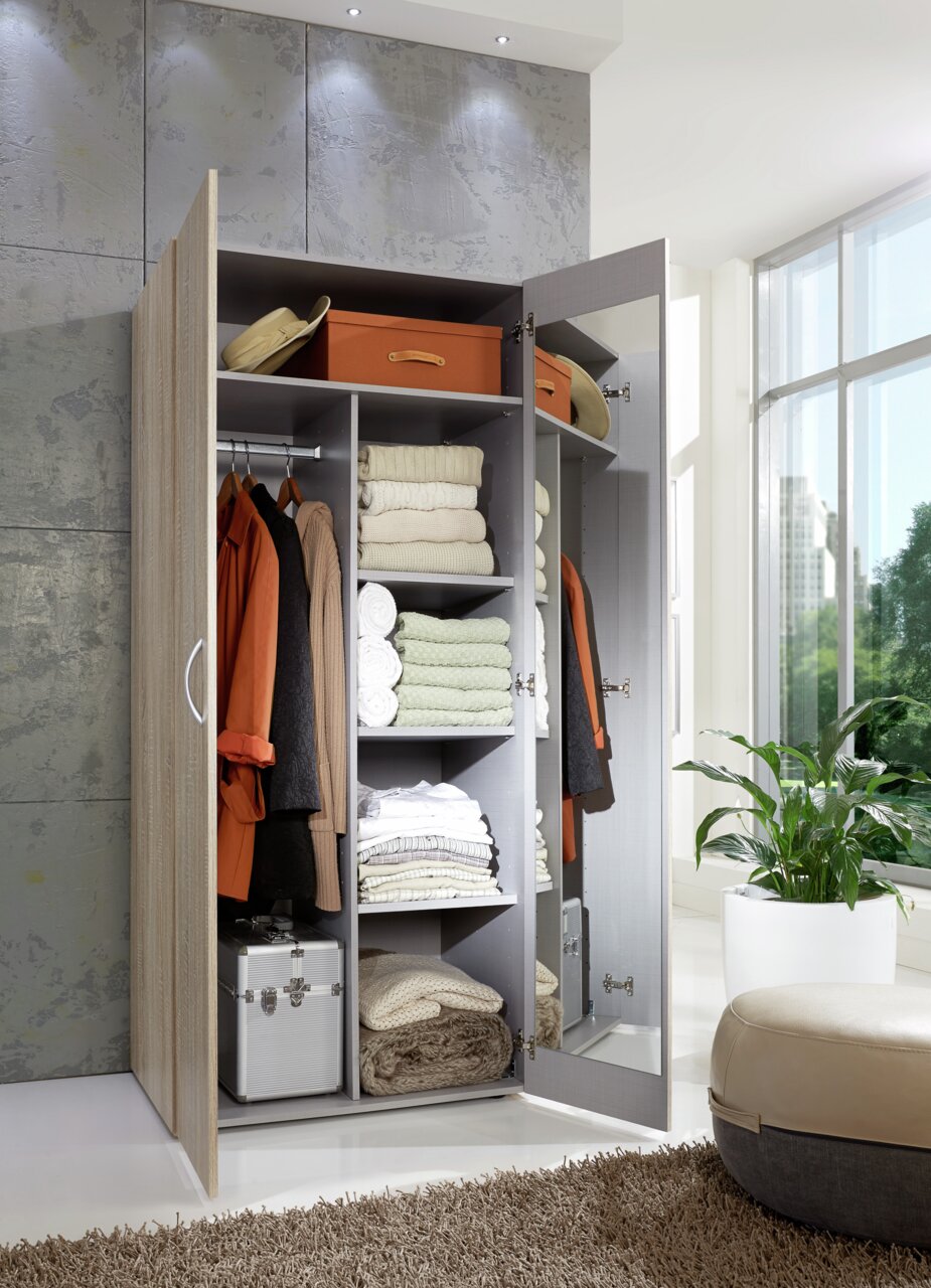 Offener Kleiderschrank mit mehreren Fächern, gefüllt mit Kleidung, Handtüchern und Aufbewahrungsboxen, aus der Perspektive von vorne rechts.