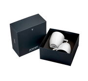 Zwei weiße Becher mit Henkel in einer eleganten schwarzen Geschenkbox von oben betrachtet.