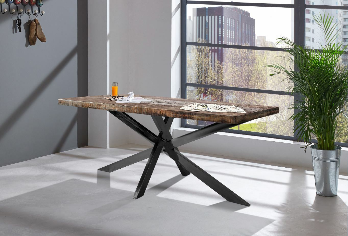 Moderner Esstisch mit rustikaler Holzplatte und schwarzem Metallgestell, seitliche Perspektive in einem hellen Raum mit großen Fenstern.