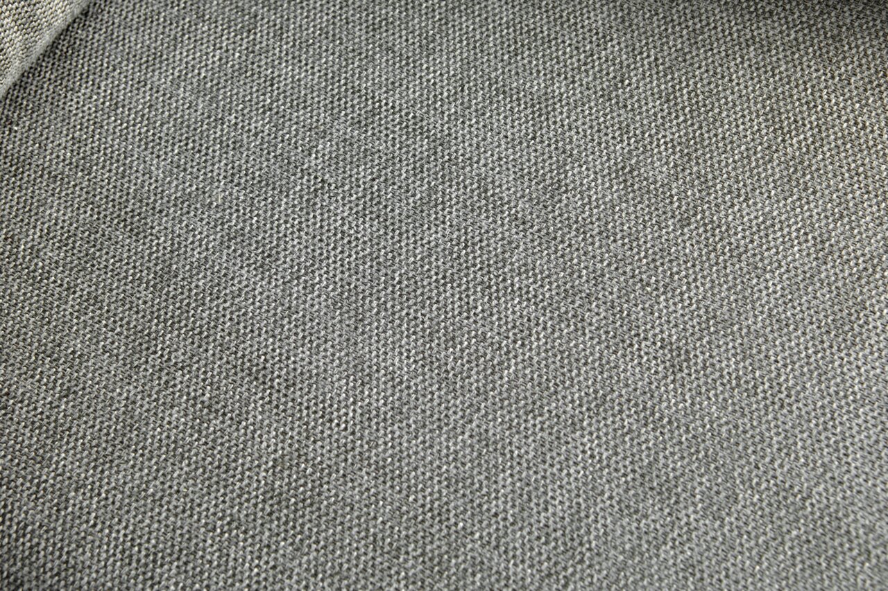 Nahaufnahme eines grauen Stoffbezugs mit feiner Webstruktur, perspektivisch von oben fotografiert.