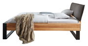 Seitliche Ansicht eines modernen Balkenbetts aus Holz mit schwarzem Metallrahmen und gepolstertem Kopfteil, dekoriert mit Kissen und einer Decke.