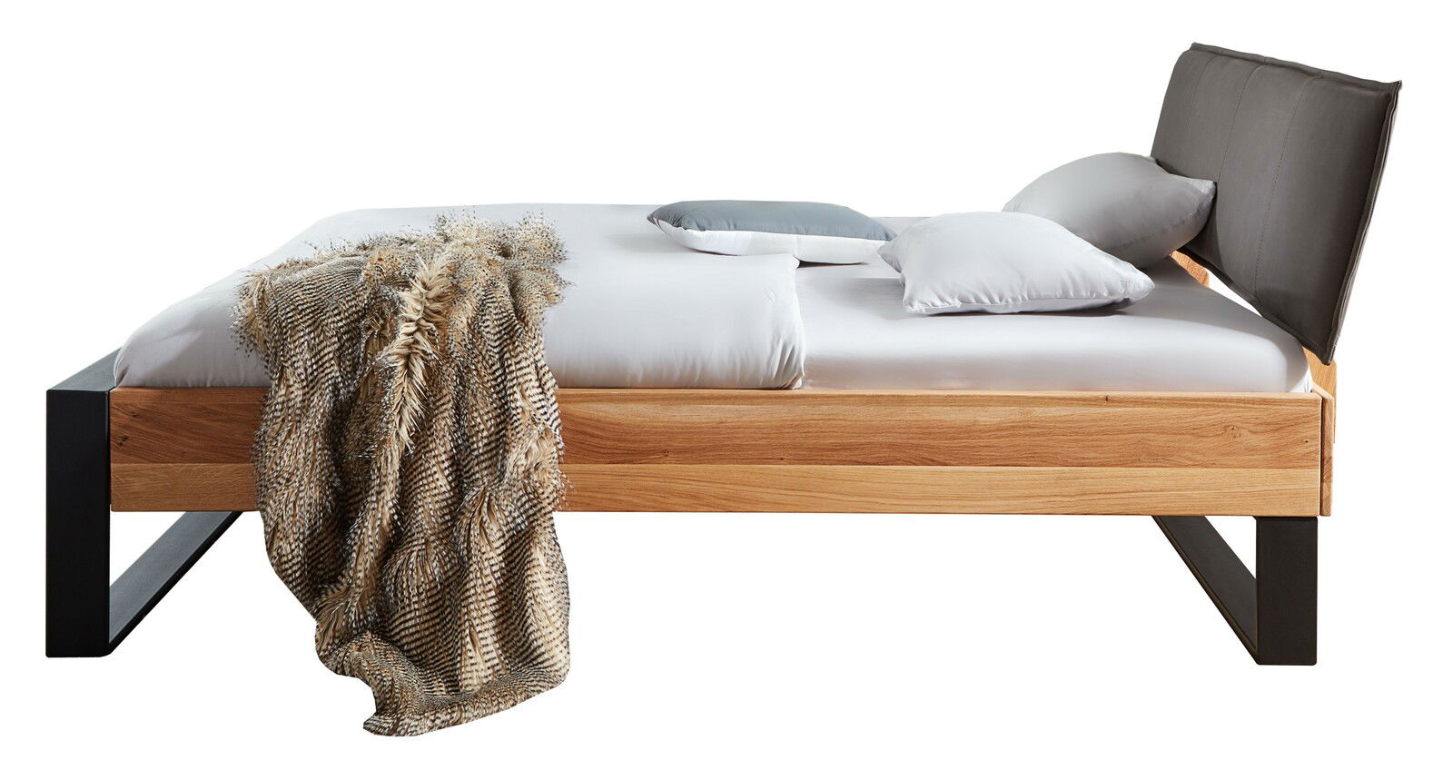 Seitliche Ansicht eines modernen Balkenbetts aus Holz mit schwarzem Metallrahmen und gepolstertem Kopfteil, dekoriert mit Kissen und einer Decke.