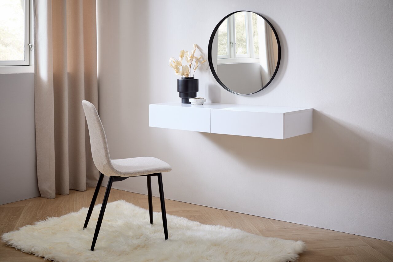 Moderne Wandkonsole in Weiß mit rundem Spiegel darüber, seitliche Perspektive. Dekoriert mit einer Vase und einem kleinen Objekt, daneben ein beiger Stuhl auf einem flauschigen Teppich.