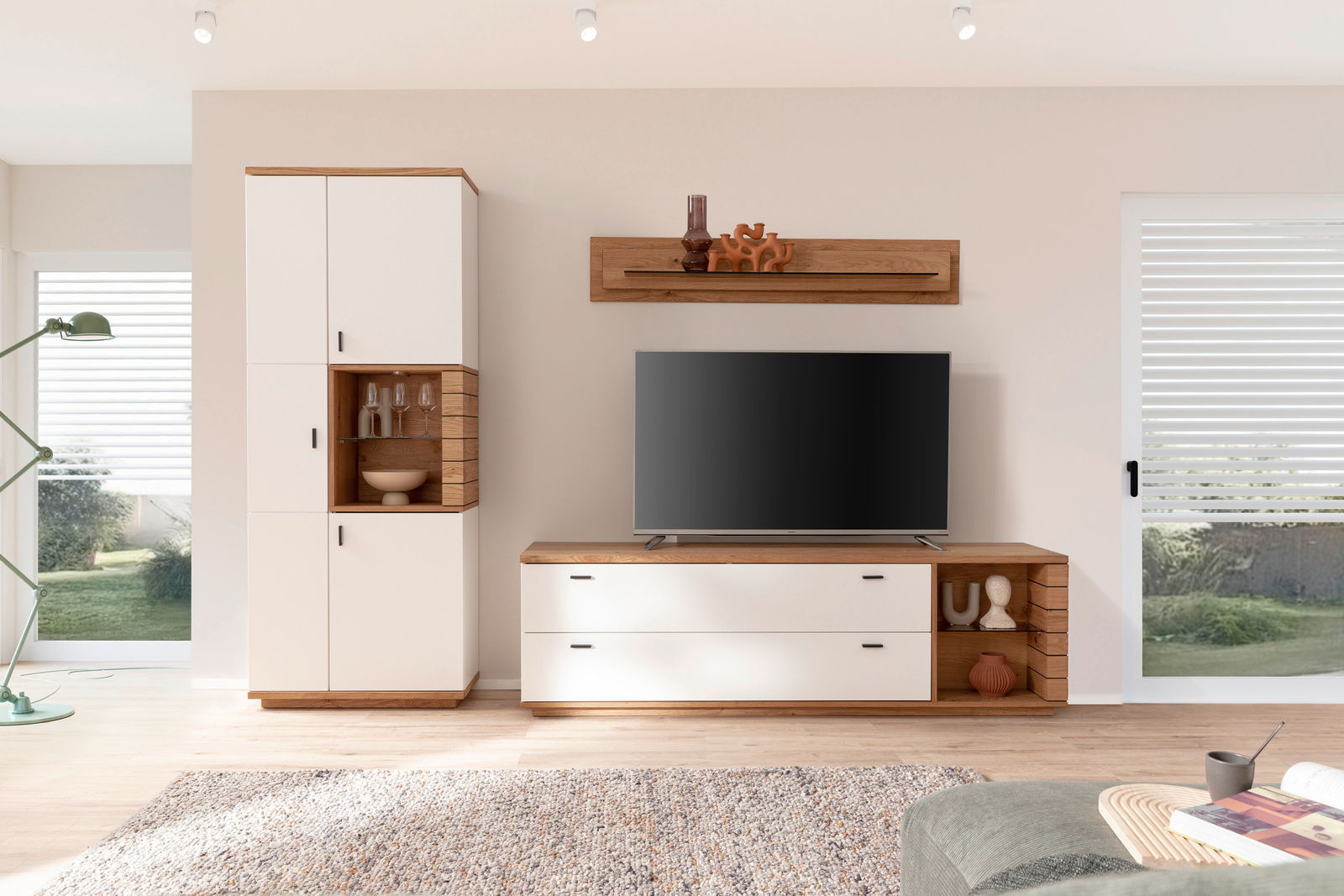 Moderne Wandkombination MANITOBA in hellem Raum, bestehend aus einem hohen Schrank, einem TV-Board und einem Wandregal, aus Holz und weißen Elementen, frontal betrachtet.