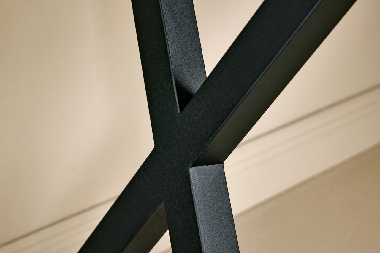 Nahaufnahme eines schwarzen Metallgestells in X-Form, Teil einer Eck-Schreibtisch-Kombination, seitliche Perspektive