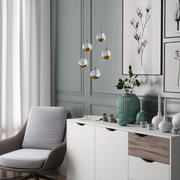 Moderne LED-Hängeleuchte von Dieter Knoll mit fünf kugelförmigen, gold- und silberfarbenen Lampenschirmen, hängend in einem stilvoll eingerichteten Wohnzimmer. Perspektive: seitlich.