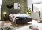 Modern gestoffeerd bed in een stijlvol ingerichte slaapkamer, zijaanzicht, met sierkussens en dekens.