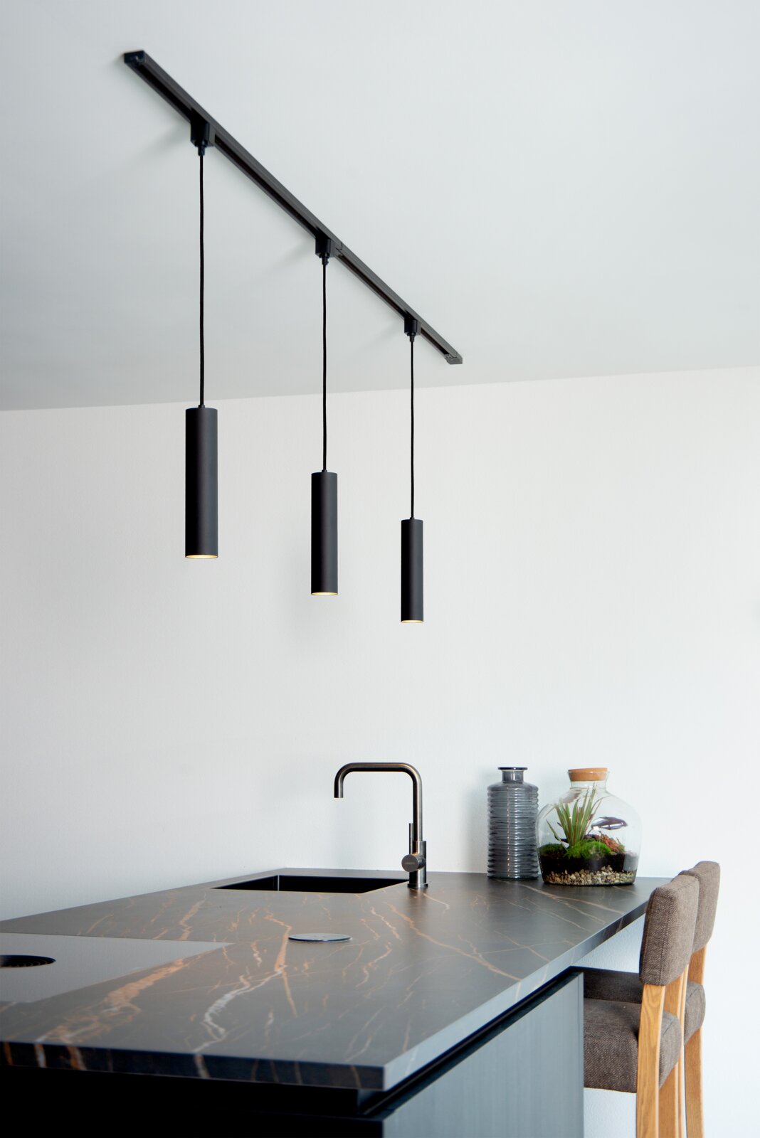 Moderne schwarze Pendelleuchte FLORIS mit drei zylindrischen Lampenschirmen, von der Decke hängend über einer stilvollen Kücheninsel. Seitliche Perspektive.