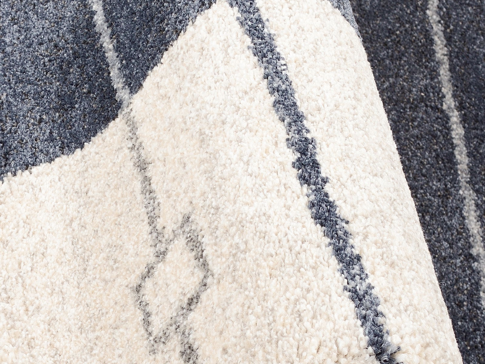 Nahaufnahme eines Frisé-Teppichs mit geometrischem Muster in Weiß und Dunkelblau, diagonale Perspektive.