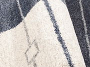 Nahaufnahme eines Frisé-Teppichs mit geometrischem Muster in Weiß und Dunkelblau, diagonale Perspektive.