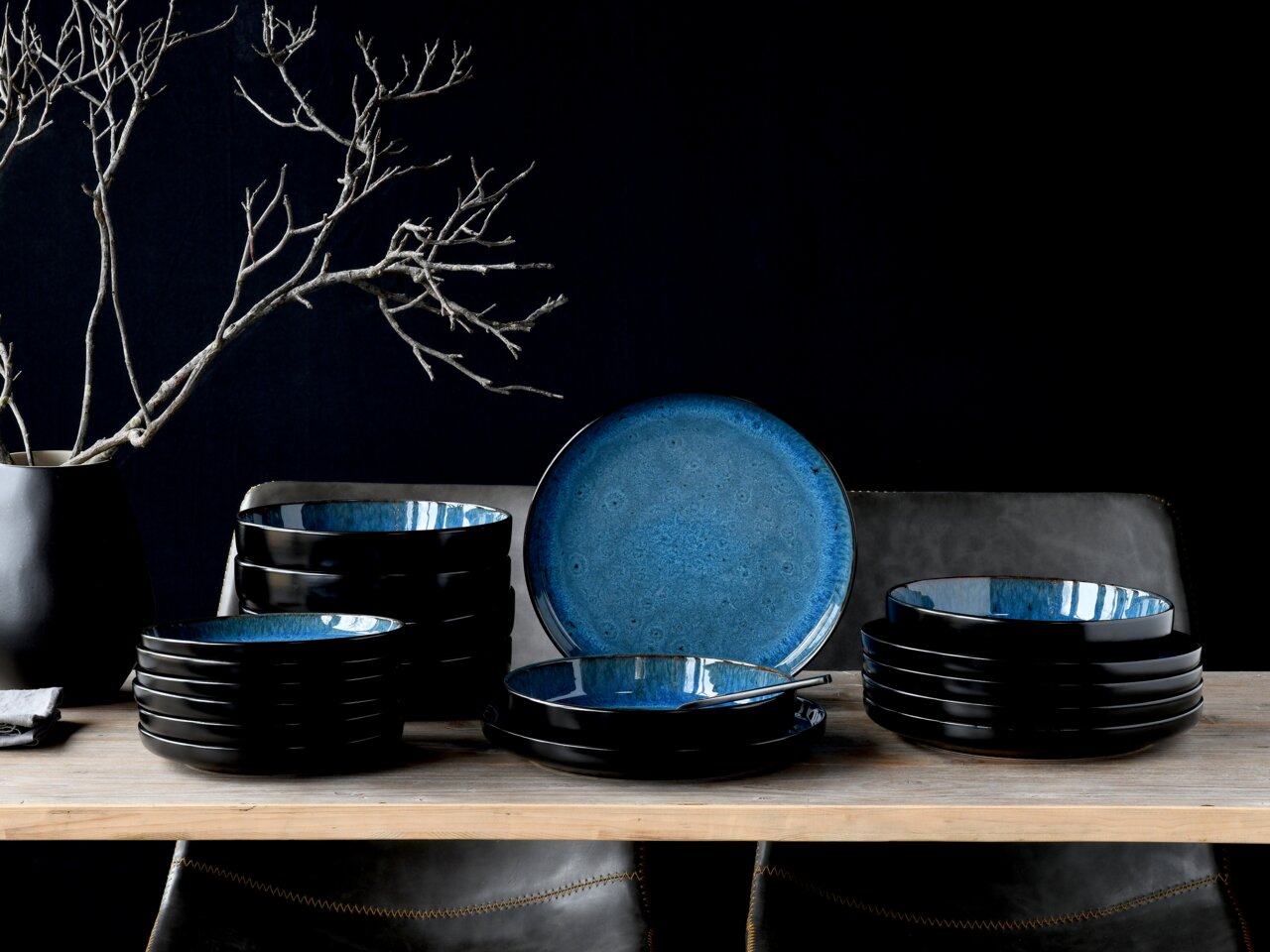 Elegantes 18-teiliges Tellerset in Blau, präsentiert auf einem Tisch aus der Seitenperspektive, mit einem modernen, dunklen Design und einem dekorativen Ast im Hintergrund.