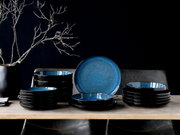 Elegantes 18-teiliges Tellerset in Blau, präsentiert auf einem Tisch aus der Seitenperspektive, mit einem modernen, dunklen Design und einem dekorativen Ast im Hintergrund.