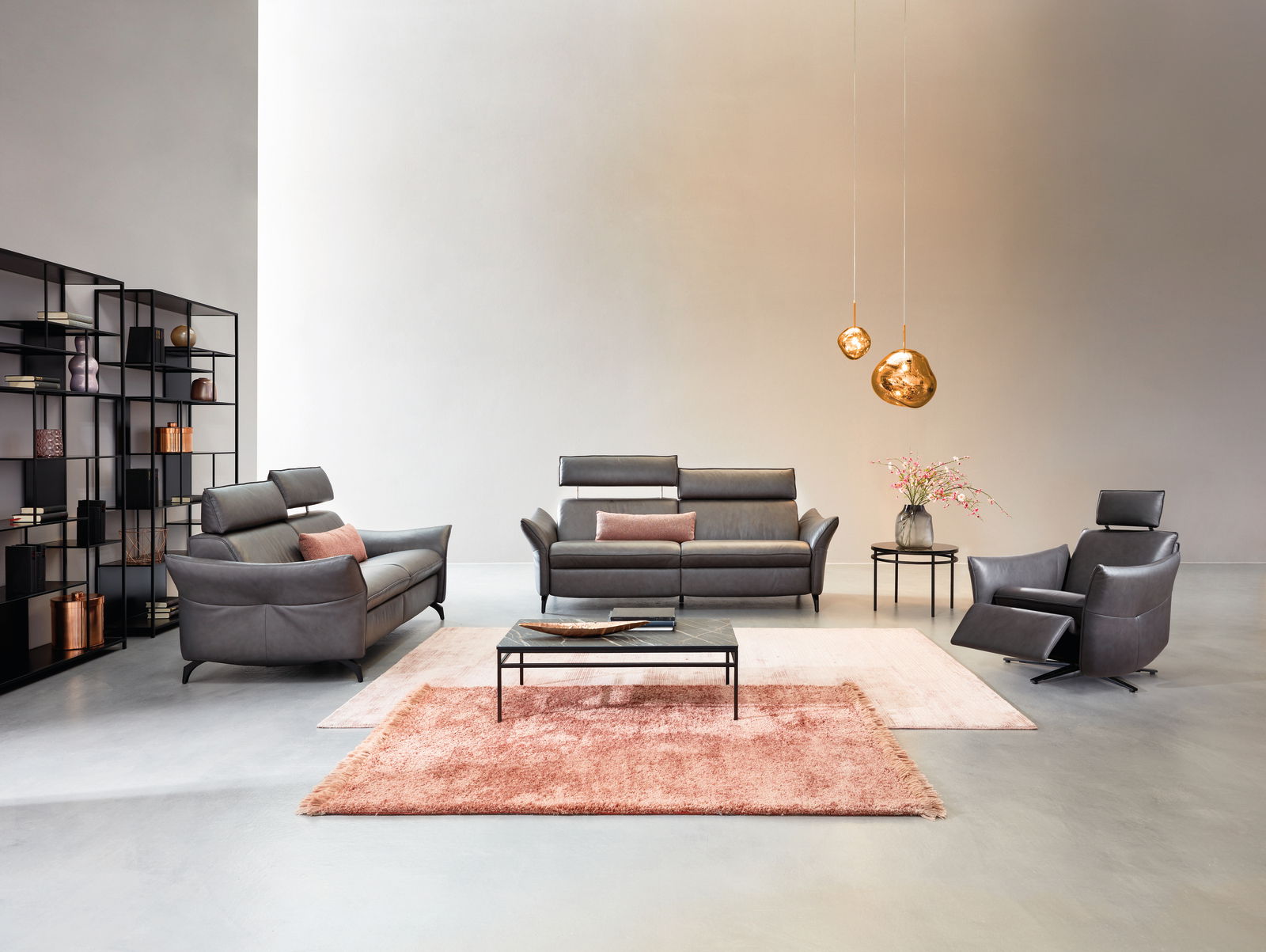 Wohnzimmeransicht mit Himolla Sofa PLANOPOLY MOTION, bestehend aus einem 3er-Sofa, einem 2,5er-Sofa und einem Sessel in dunklem Leder. Moderne Einrichtung mit Teppichen, Couchtisch und dekorativen Hängelampen.