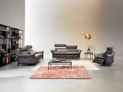 Wohnzimmeransicht mit Himolla Sofa PLANOPOLY MOTION, bestehend aus einem 3er-Sofa, einem 2,5er-Sofa und einem Sessel in dunklem Leder. Moderne Einrichtung mit Teppichen, Couchtisch und dekorativen Hängelampen.