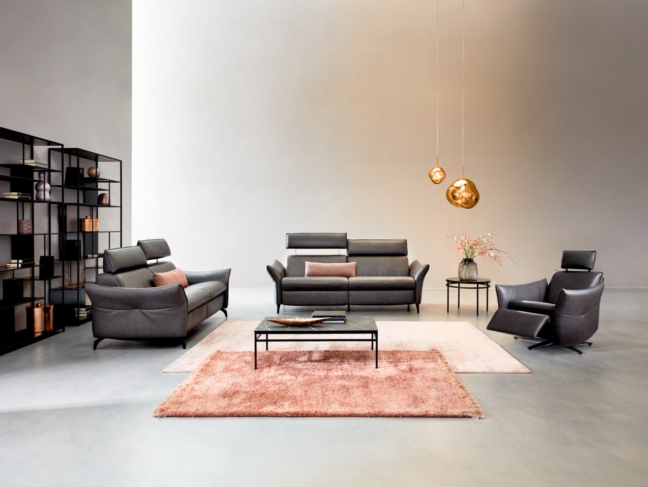 Wohnzimmeransicht mit Himolla Sofa PLANOPOLY MOTION, bestehend aus einem 3er-Sofa, einem 2,5er-Sofa und einem Sessel in dunklem Leder. Moderne Einrichtung mit Teppichen, Couchtisch und dekorativen Hängelampen.