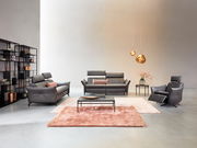 Wohnzimmeransicht mit Himolla Sofa PLANOPOLY MOTION, bestehend aus einem 3er-Sofa, einem 2,5er-Sofa und einem Sessel in dunklem Leder. Moderne Einrichtung mit Teppichen, Couchtisch und dekorativen Hängelampen.