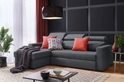 Graues Ecksofa mit roten und gemusterten Kissen, dekoriert mit einer Decke, in einem modernen Wohnzimmer mit Pflanzen und einem Couchtisch, seitliche Perspektive.